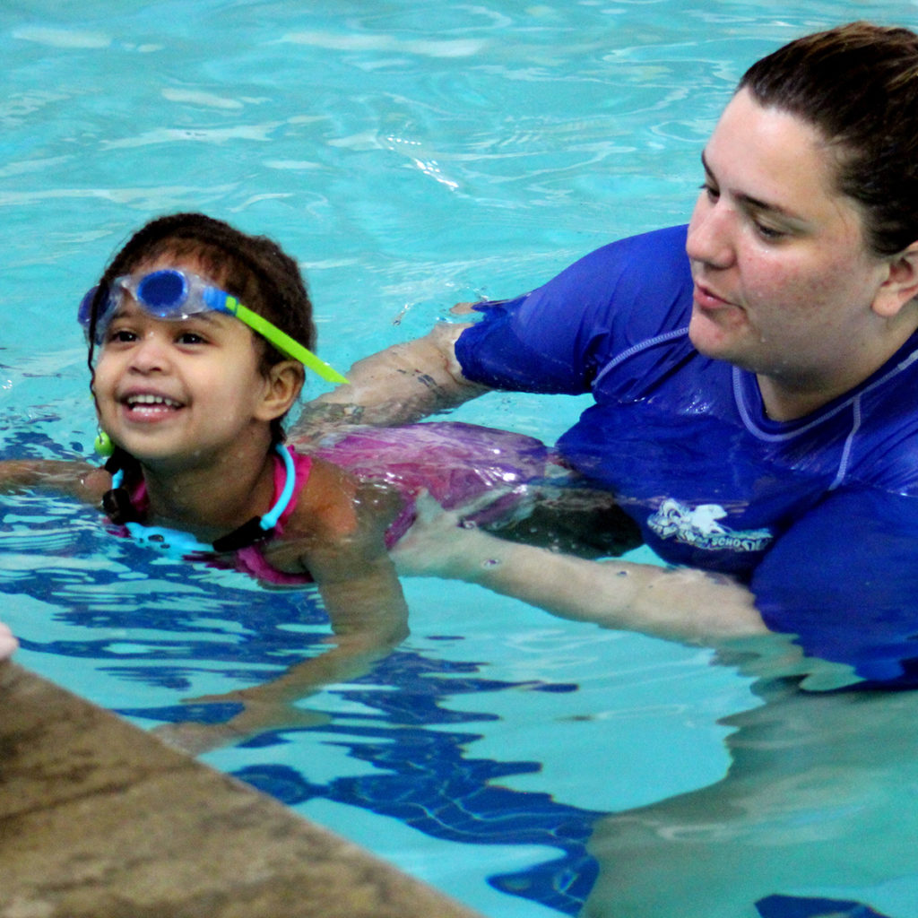 A swim instructor is helping a young swimmer to the wall. The swim instructor is holding the student around the waist and the student has their head above the water.