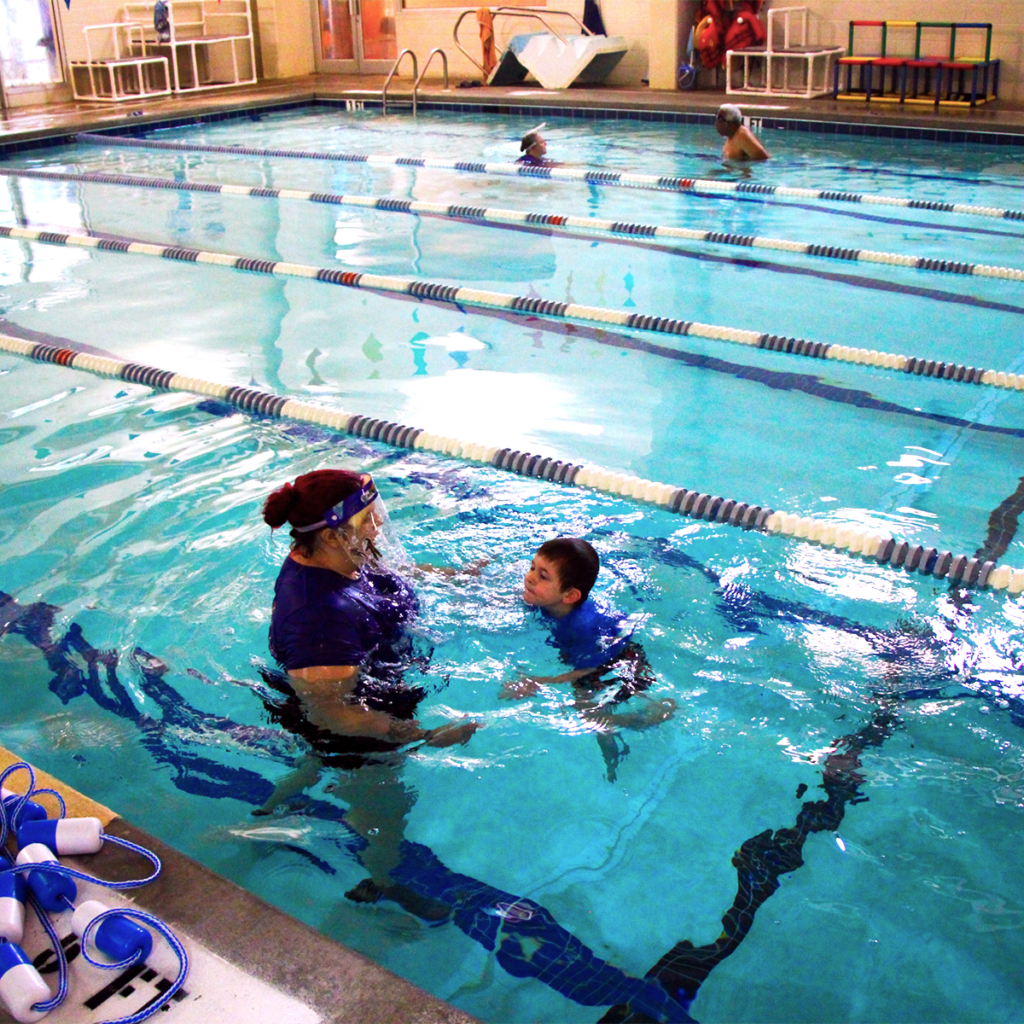 A student is practicing his treading water as a teacher stand beside him, close enough to grab but leaving her hands away from him so he can practice.