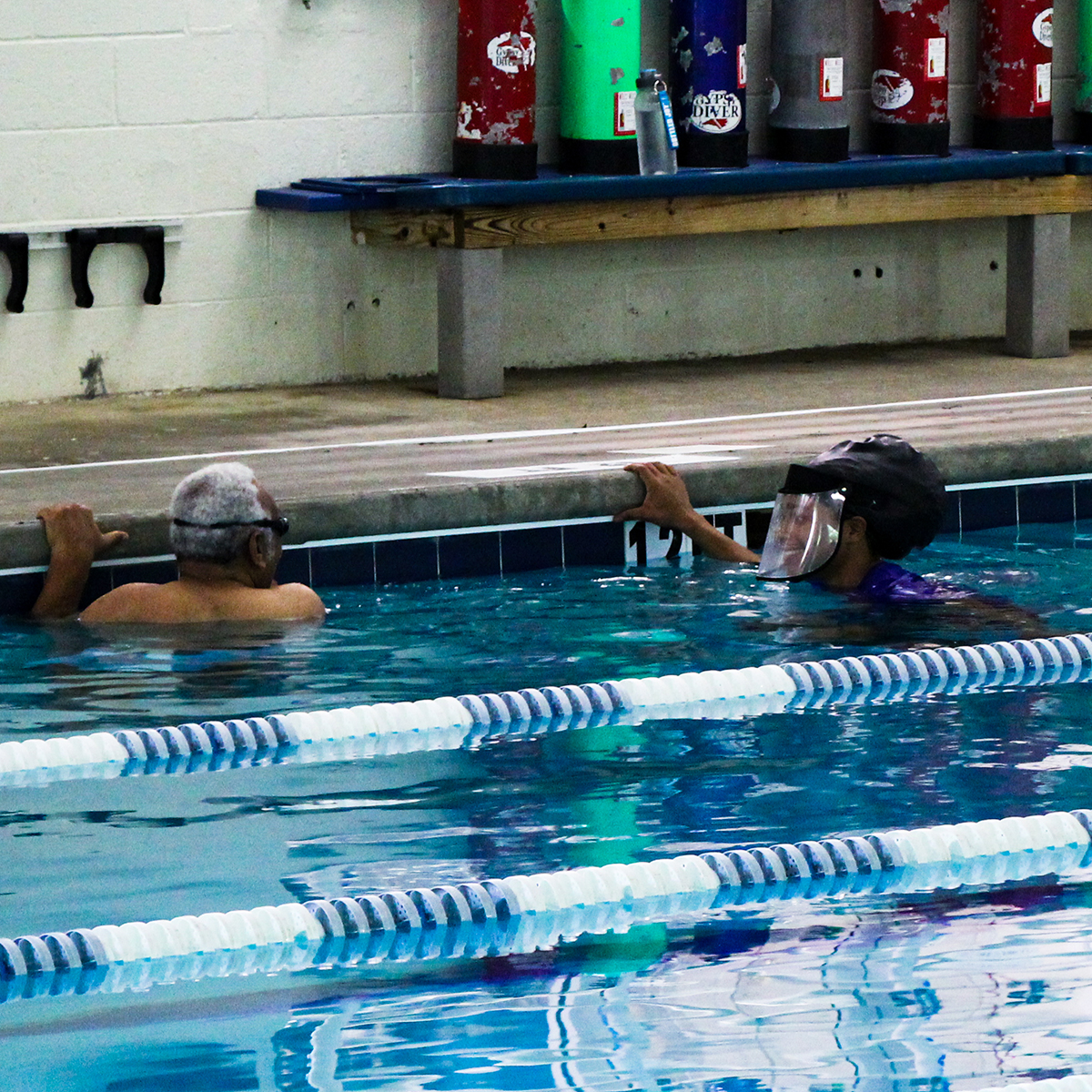 Instructor and student laughing while holding onto the wall in the deep end